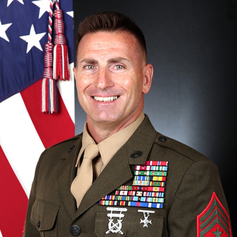 A man dressed in a military dress uniform smiles for a portrait.