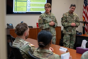 Women and man standing in front of two soldiers sitting down.