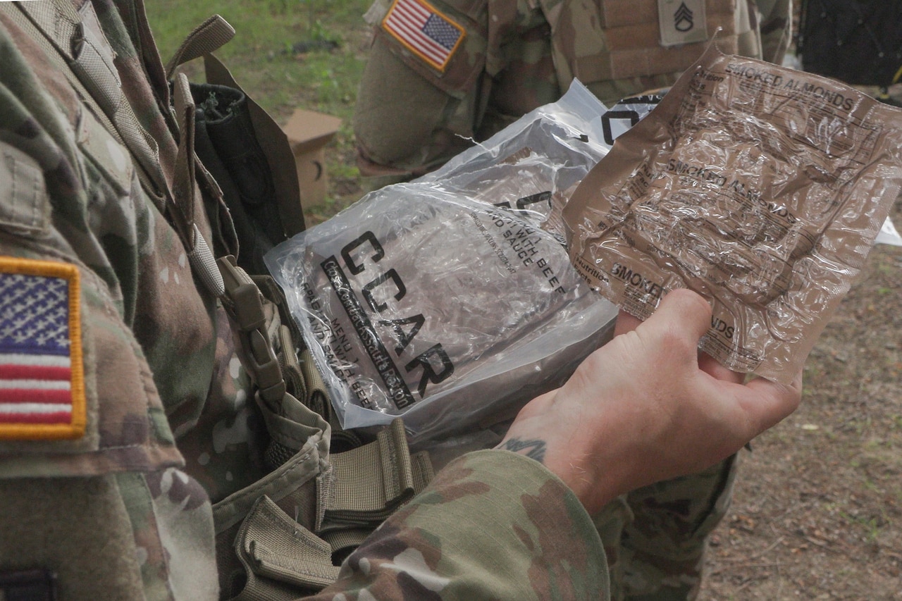 A person wearing a military camouflage uniform looks at two small plastic packages in their hands.