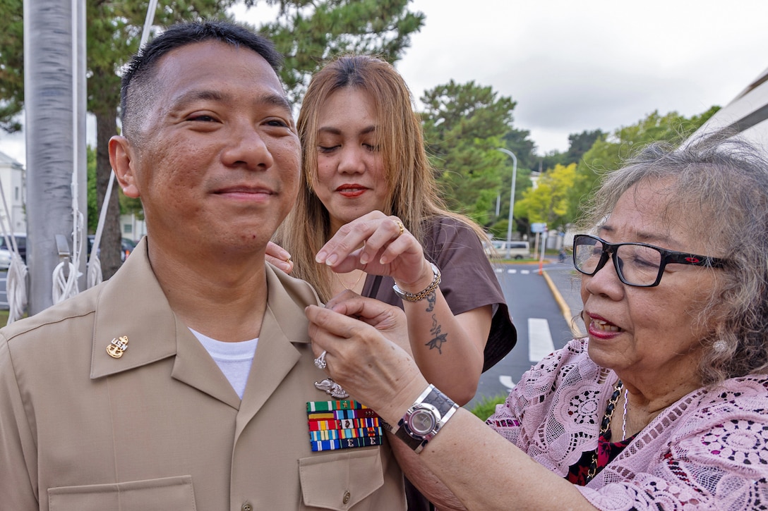 Two loved ones smile as they pin an anchor to a sailor's lapel.
