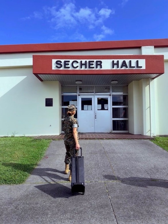 A Marine carries a black rolling piece of equipment into Secher Hall