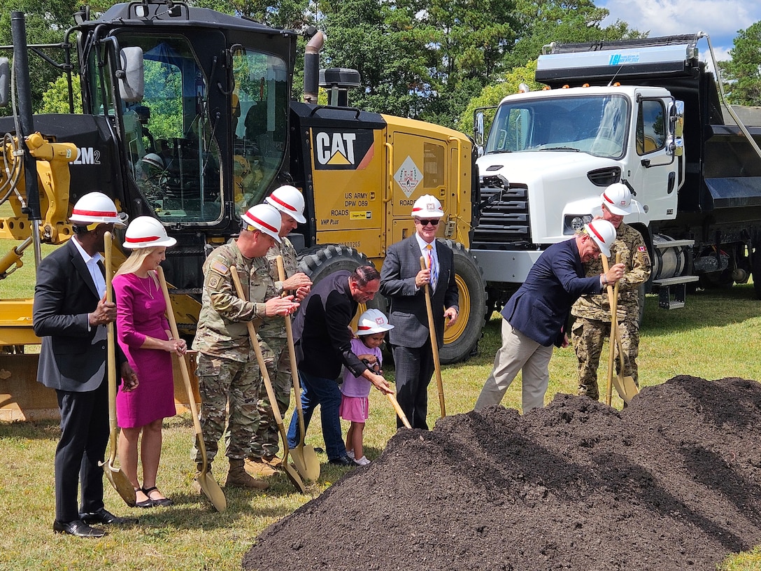 Photo of people with shovels and dirt with construction trucks and machinery in the background.