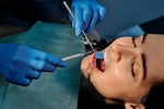 Woman wearing dental bib opens her mouth as a dentist uses dental equipment.