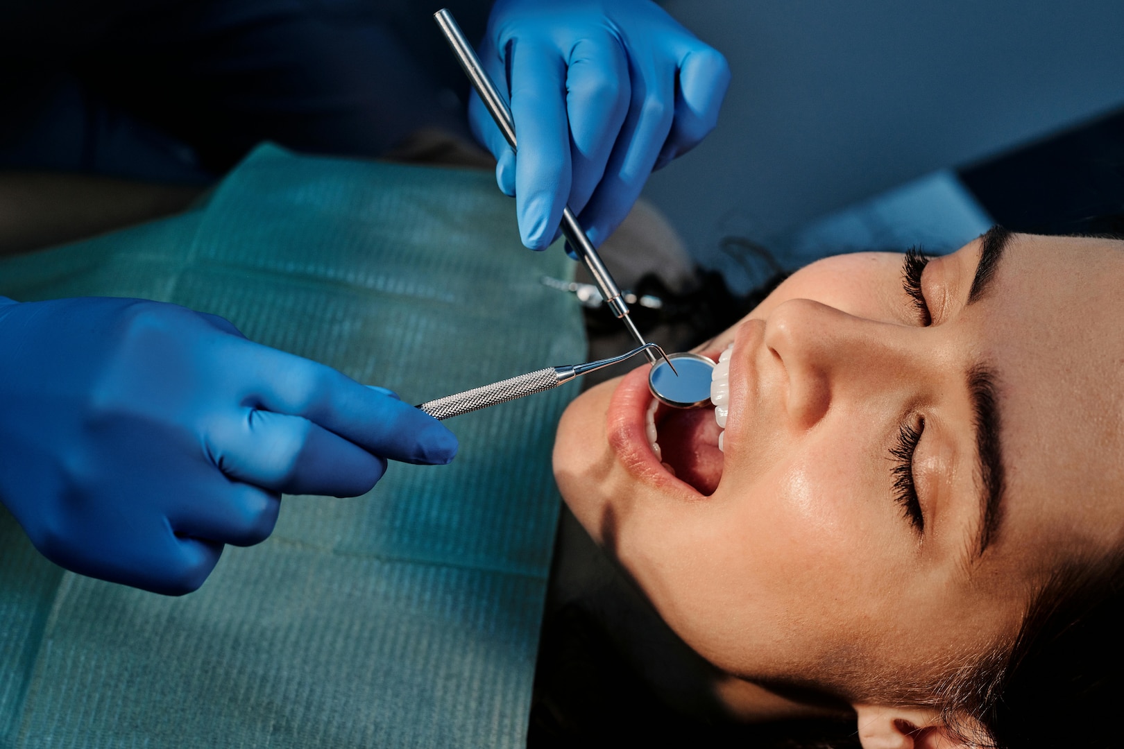 Woman wearing dental bib opens her mouth as a dentist uses dental equipment.