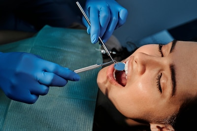 Woman wearing dental bib opens her mouth as a dentist uses dental equipment.
