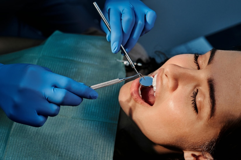 Woman wearing dental bib opens her mouth as a dentist uses dental equipment.