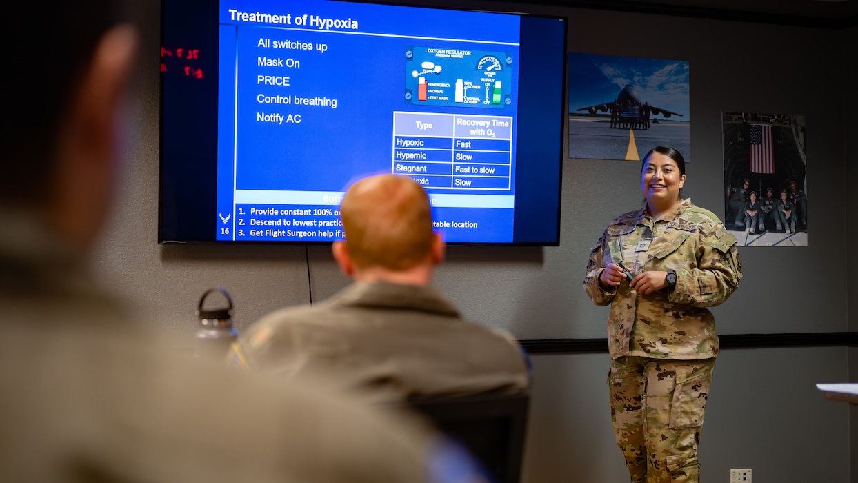An Airman stands by a projector in a classroom while teaching a class