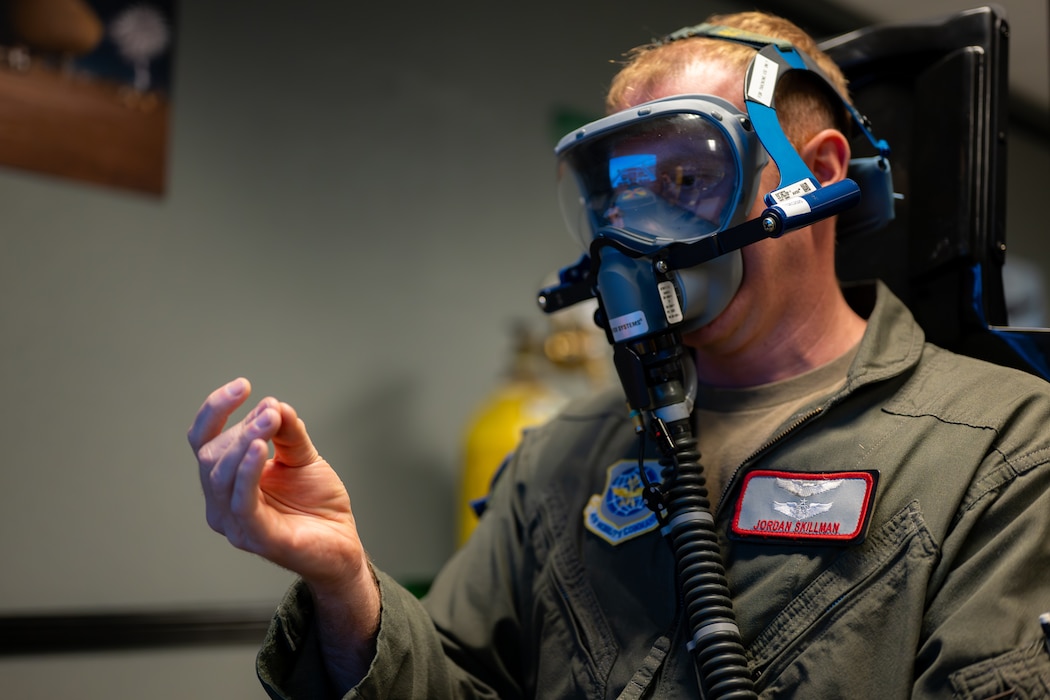 An airman presses fingers together with his right hand with a mask on