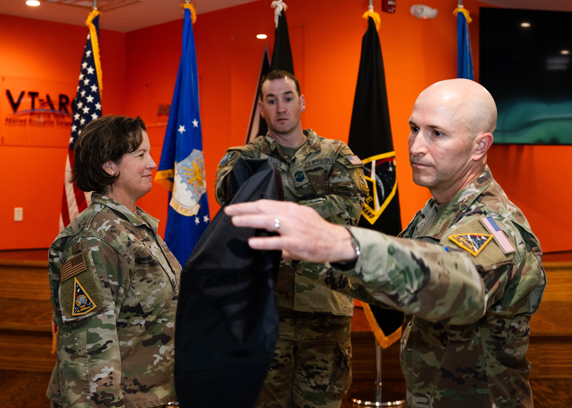 USAF Brig. Gen. Michelle Idle (left), mobilization assistant to the SSC commander, USSF SMSgt. Justin Creger  (middle), System Delta (SYD) 81 senior enlisted leader and USSF Col. Corey Klopstein (right), SYD 81 commander, participate in the unfurling of the SYD 81 guidon at a ceremony in Colorado Springs, Colo. on Sept. 9, 2025. (USAF Photo by Senior Airman William Pugh)