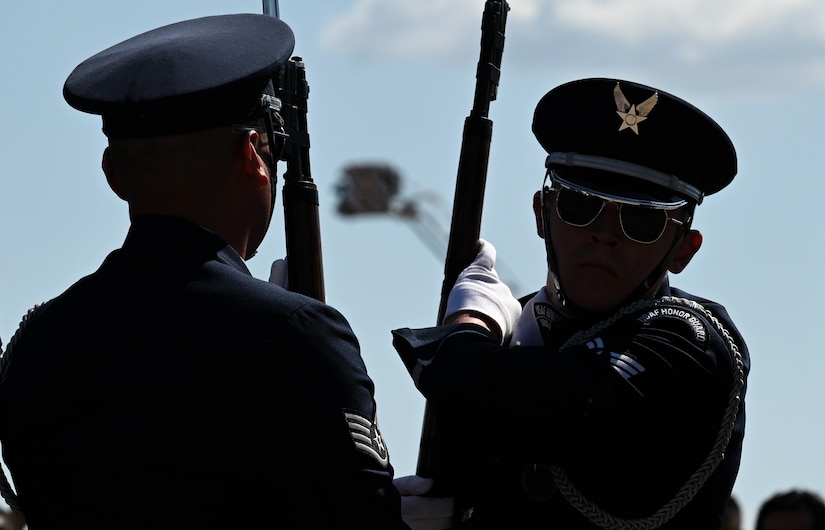 Two Airmen dressed in honor guard uniforms hold rifles while performing.