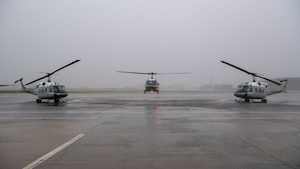 One UH-1N Huey prepares to land as two UH-1N Huey's are parked on the ground.