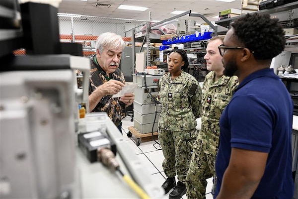 Inside a well-equipped laboratory, a Navy instructor provides guidance to a sailor working on electronic equipment. This image depicts the hands-on training environment at NIWC Atlantic designed to improve radio communication skills.