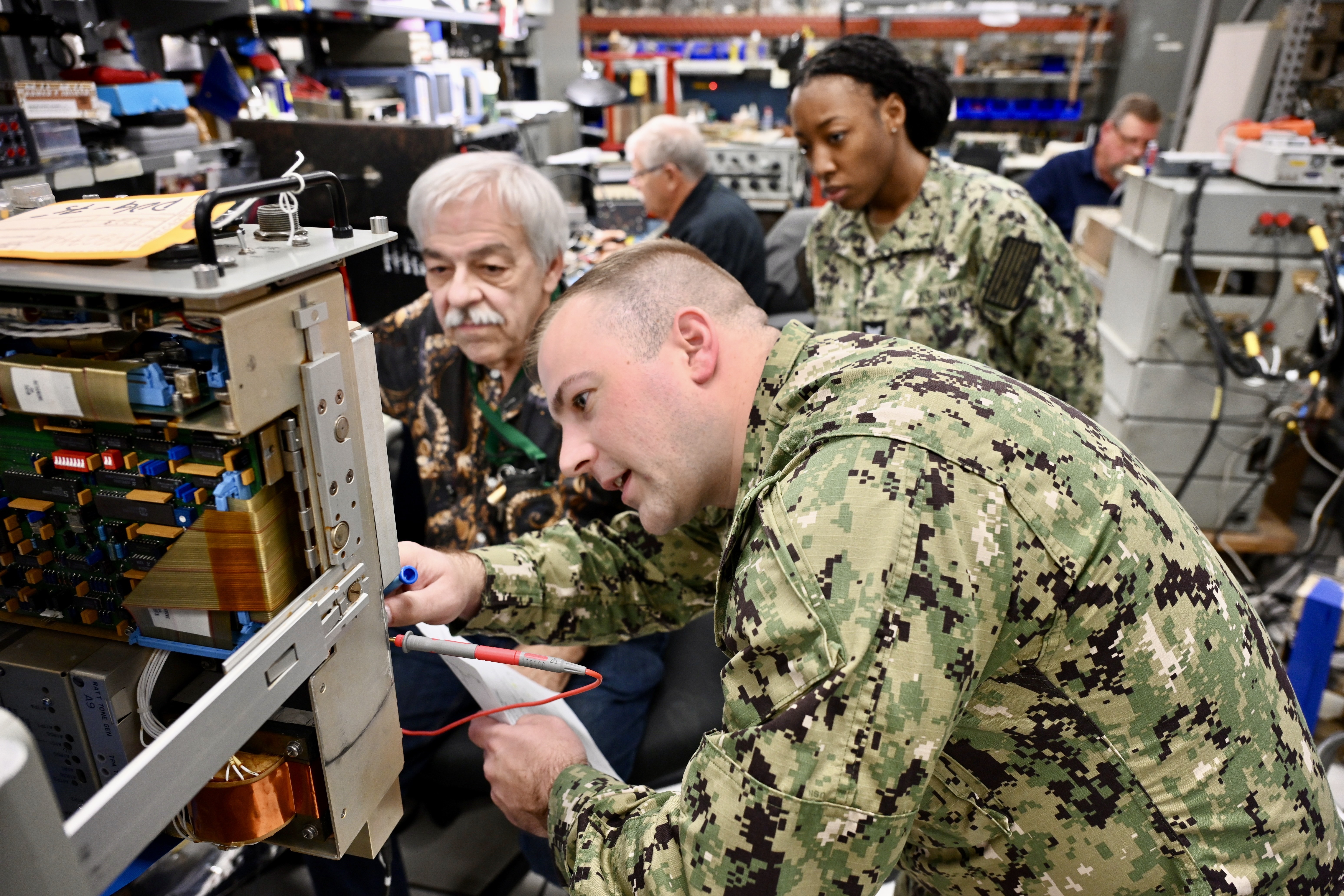 A Navy Sailor is intently focused on troubleshooting electronic equipment in a lab environment, indicating the technical training being provided by NIWC Atlantic to enhance radio communication skills.