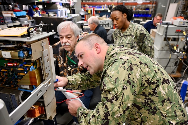 A Navy Sailor is intently focused on troubleshooting electronic equipment in a lab environment, indicating the technical training being provided by NIWC Atlantic to enhance radio communication skills.