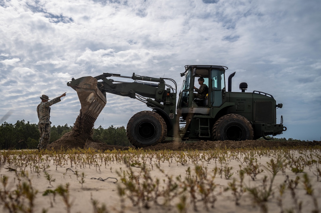 U.S. Marine Corps Lance Cpl. Alonzo Not Afraid, left, an engineer equipment operator with Combat Logistics Battalion 24, Combat Logistics Regiment 27, 2nd Marine Logistics Group,  ground guides Lance Cpl. Haysten Trinity, an engineer equipment operator with CLB-24, CLR-27, 2nd MLG, during a hasty vehicle survivability position operation as part of a battalion field exercise at Marine Corps Base Camp Lejeune, North Carolina, Sept. 13, 2025. CLB-24 conducted a battalion field exercise to sustain training and readiness standards, increase technical proficiency, and enhance the battalion’s ability to complete core mission essential tasks. Not Afraid is a native of Montana. (U.S. Marine Corps photo by Sgt. Alfonso Livrieri)