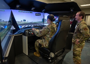 woman operates driving simulator while man observes