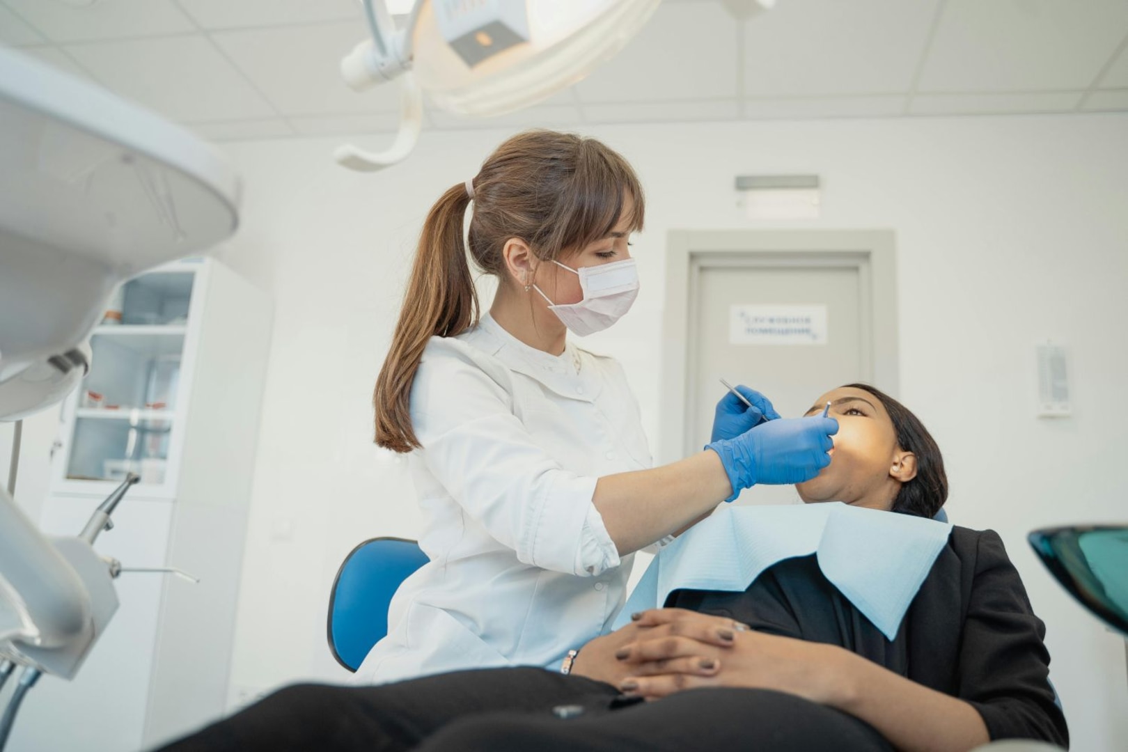 Dental care provider wearing gloves performs dental procedure on patient in dental chair.