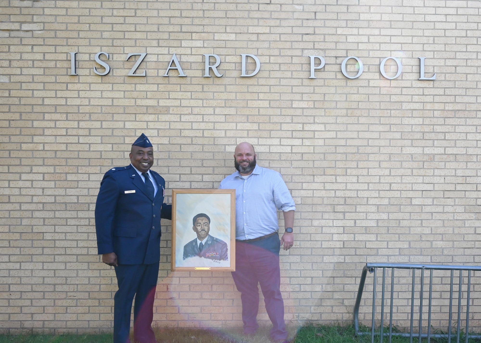 Two men holding a painting, standing at the pool facility at Tinker AFB.