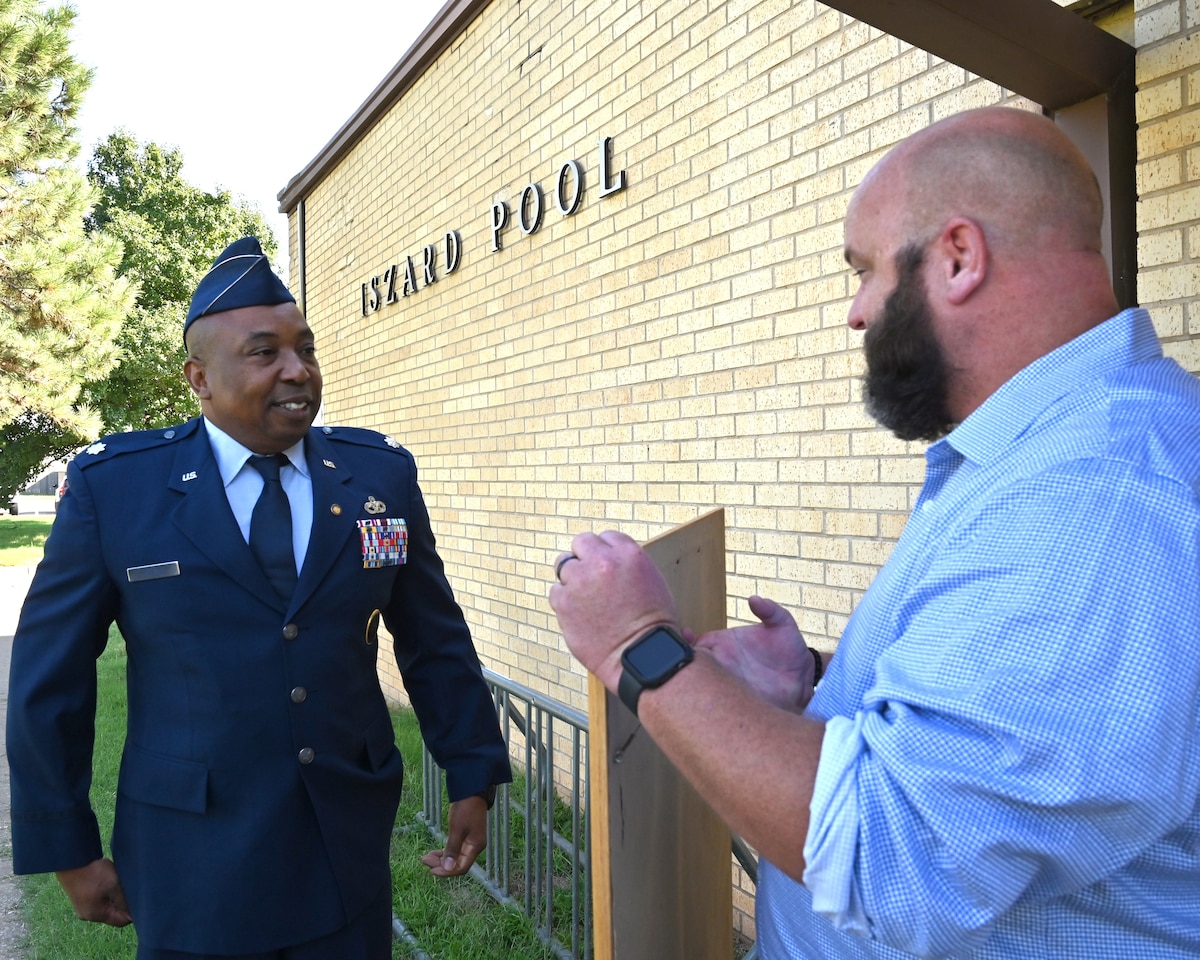 Two men holding a painting, standing at the pool facility at Tinker AFB.
