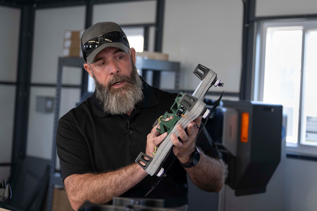 A bearded man in business casual attire holds a small drone.