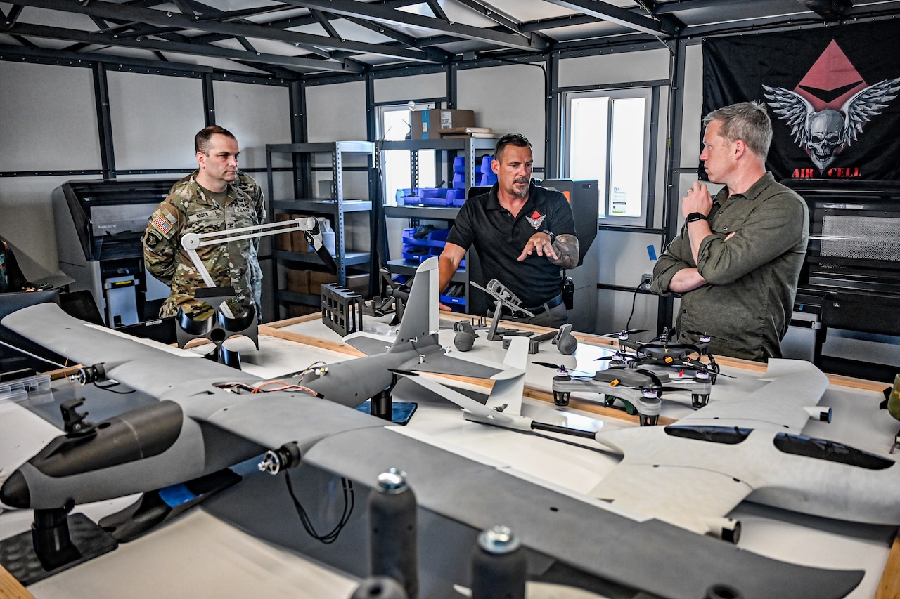 One man in business casual attire talks to another main in similar attire while pointing at a table full of drone parts.