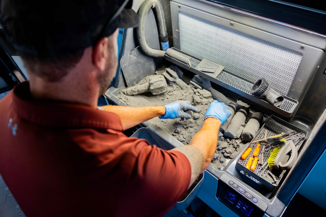 A man in gloves sifts through 3D printing powder to find the created components.
