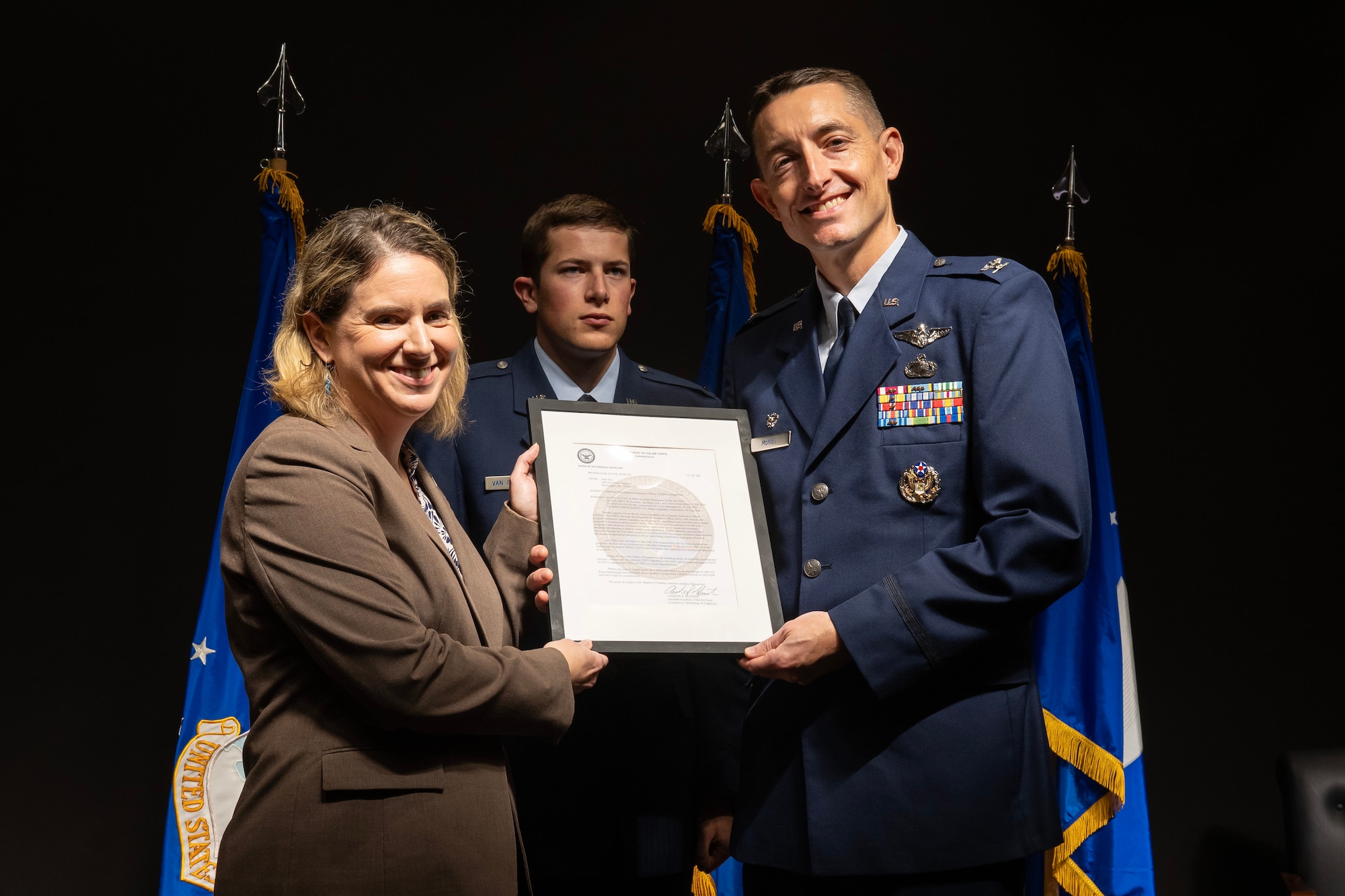 Woman in brown jacket hands citation to man in Air Force dress blues.