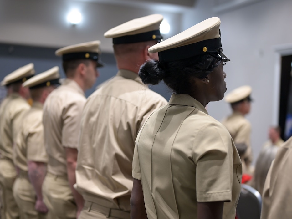 A group of Navy chief petty officers stand in a row at the position of attention as they attend the Fiscal Year 2026 Chief Petty Officer Induction Ceremony.