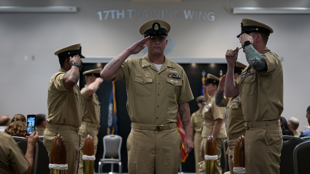 U.S. Navy Cryptologic Technician Collection Chief Petty Officer Micheal Turnage salutes the sideboys at an event. Service members salute him as he walks down the passageway.