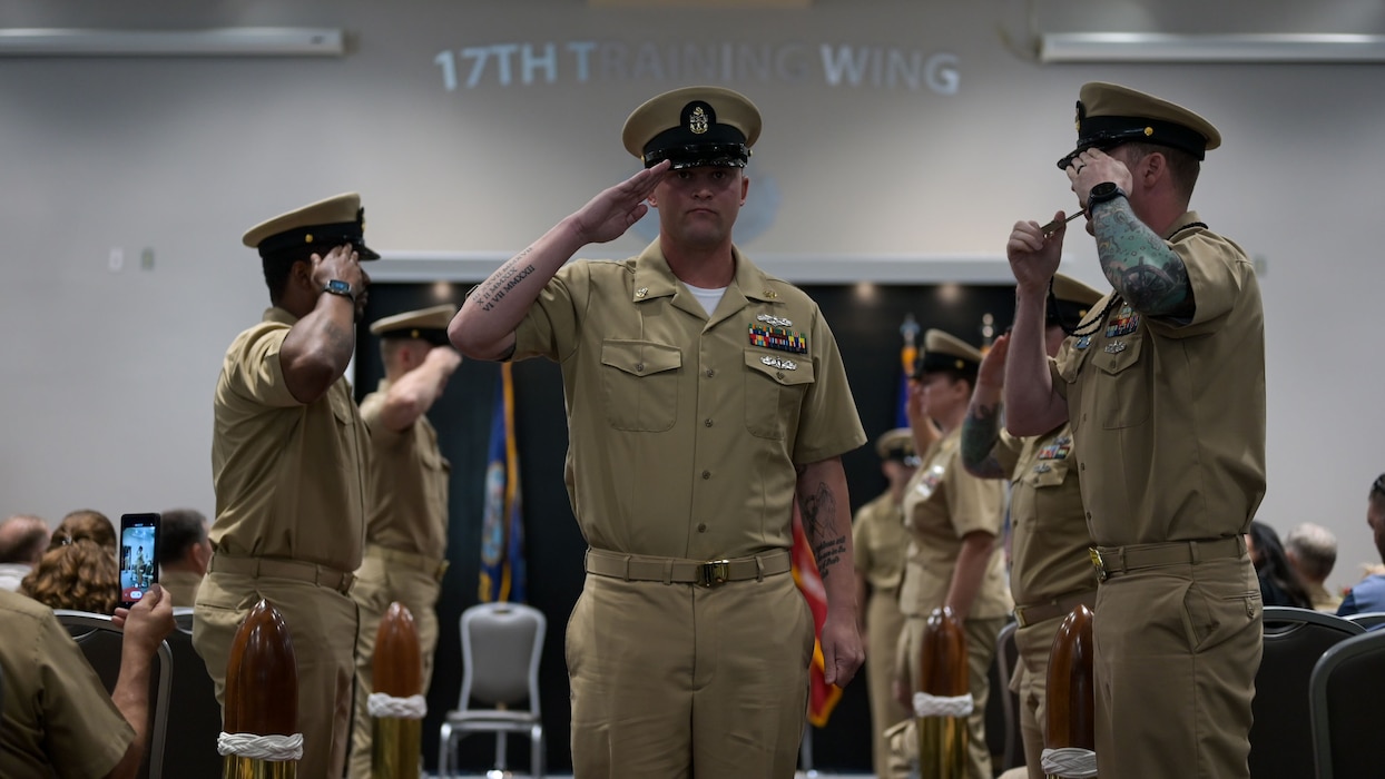 U.S. Navy Cryptologic Technician Collection Chief Petty Officer Micheal Turnage salutes the sideboys at an event. Service members salute him as he walks down the passageway.