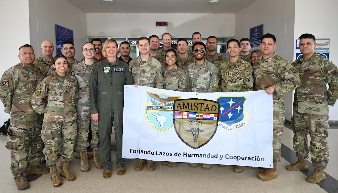 A group of U.S. military personell stand together for a group photo and hold a banner which has the SOUTHCOM logo on the left, AMISTAD logo in the middle, and the AFSOUTH logo on the right.