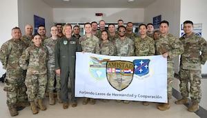 A group of U.S. military personell stand together for a group photo and hold a banner which has the SOUTHCOM logo on the left, AMISTAD logo in the middle, and the AFSOUTH logo on the right.