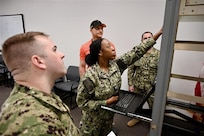 Navy reservists participate in classroom instruction on radio communication systems as part of a NIWC Atlantic training program. An instructor is visible at the front of the room.