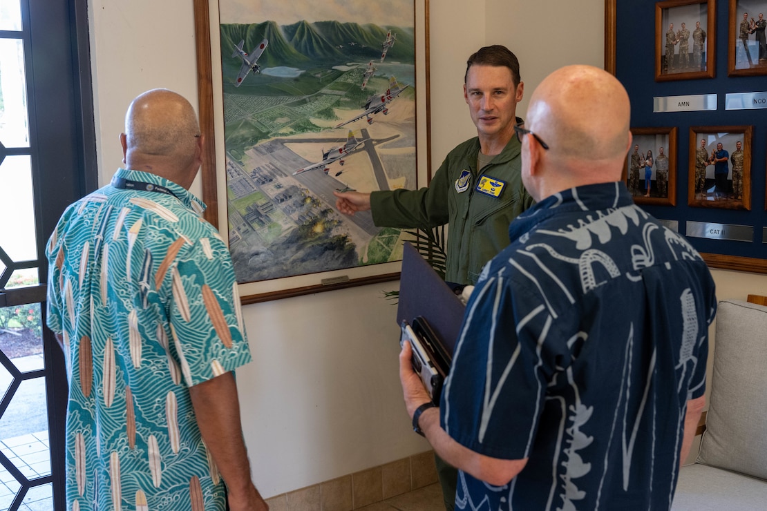 A U.S. Air Force Airmen shows two civilians a painting depicting the history of Joint Base Pearl Harbor-Hickam, Hawaii.