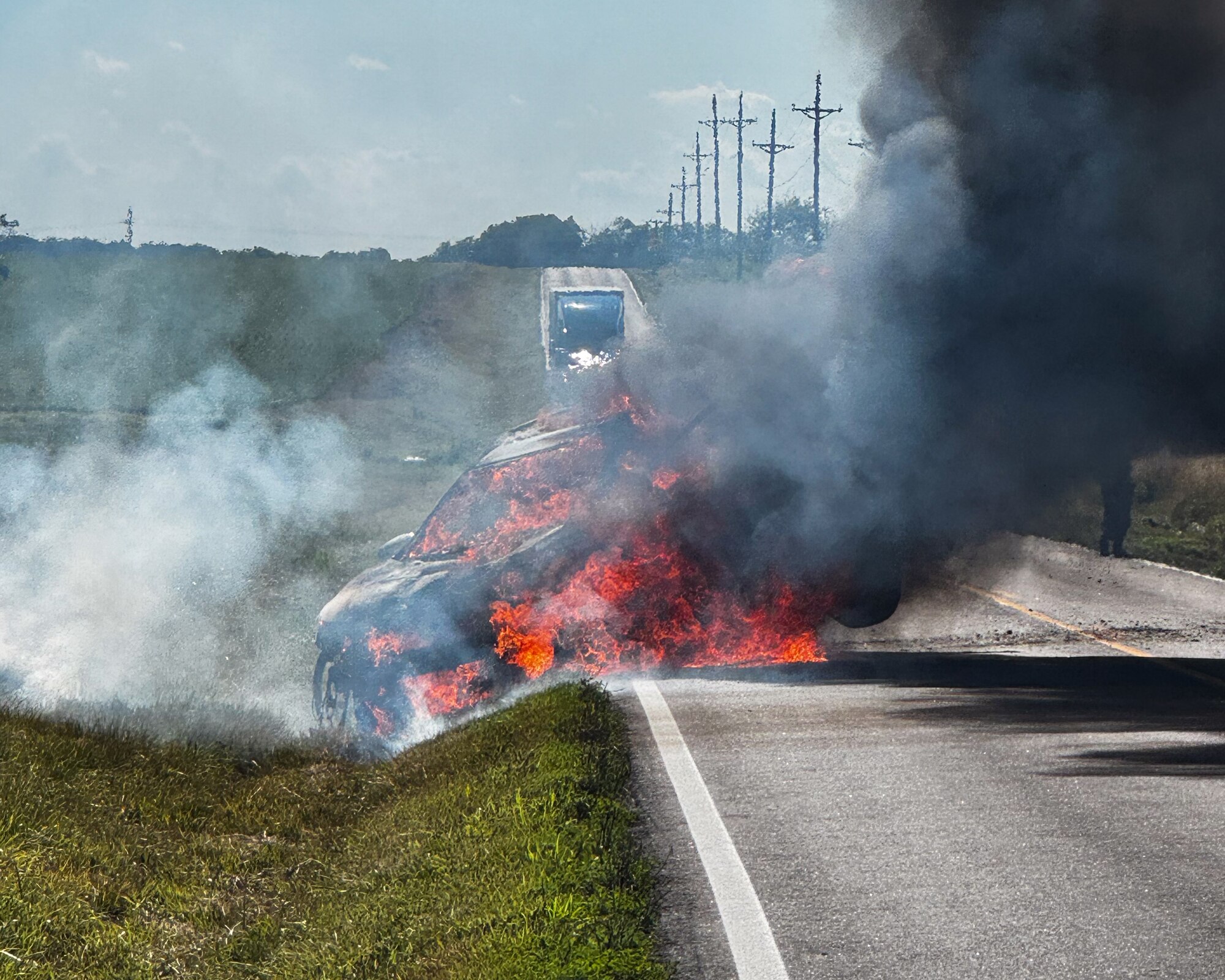 A car engulfed in flames is shown on a road near Whiteman Air Force Base, Missouri, July 9, 2025.