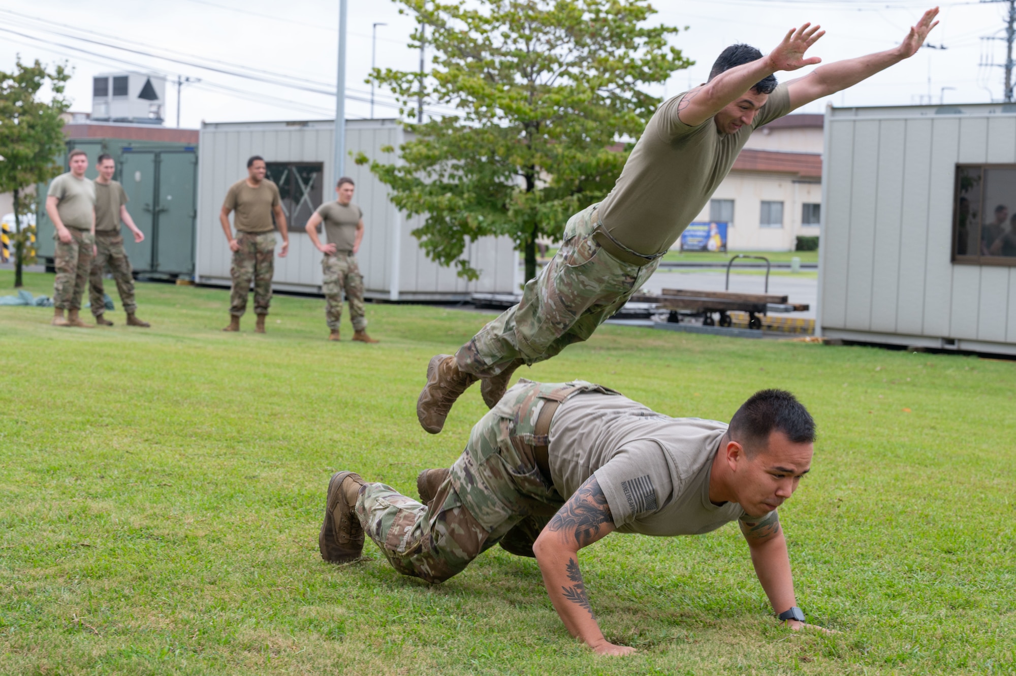 Two servicemembers perform modified burpees in a group exercise