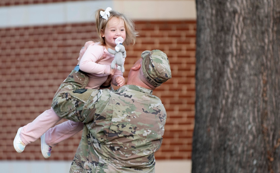 Soldier playfully tosses young daughter in air