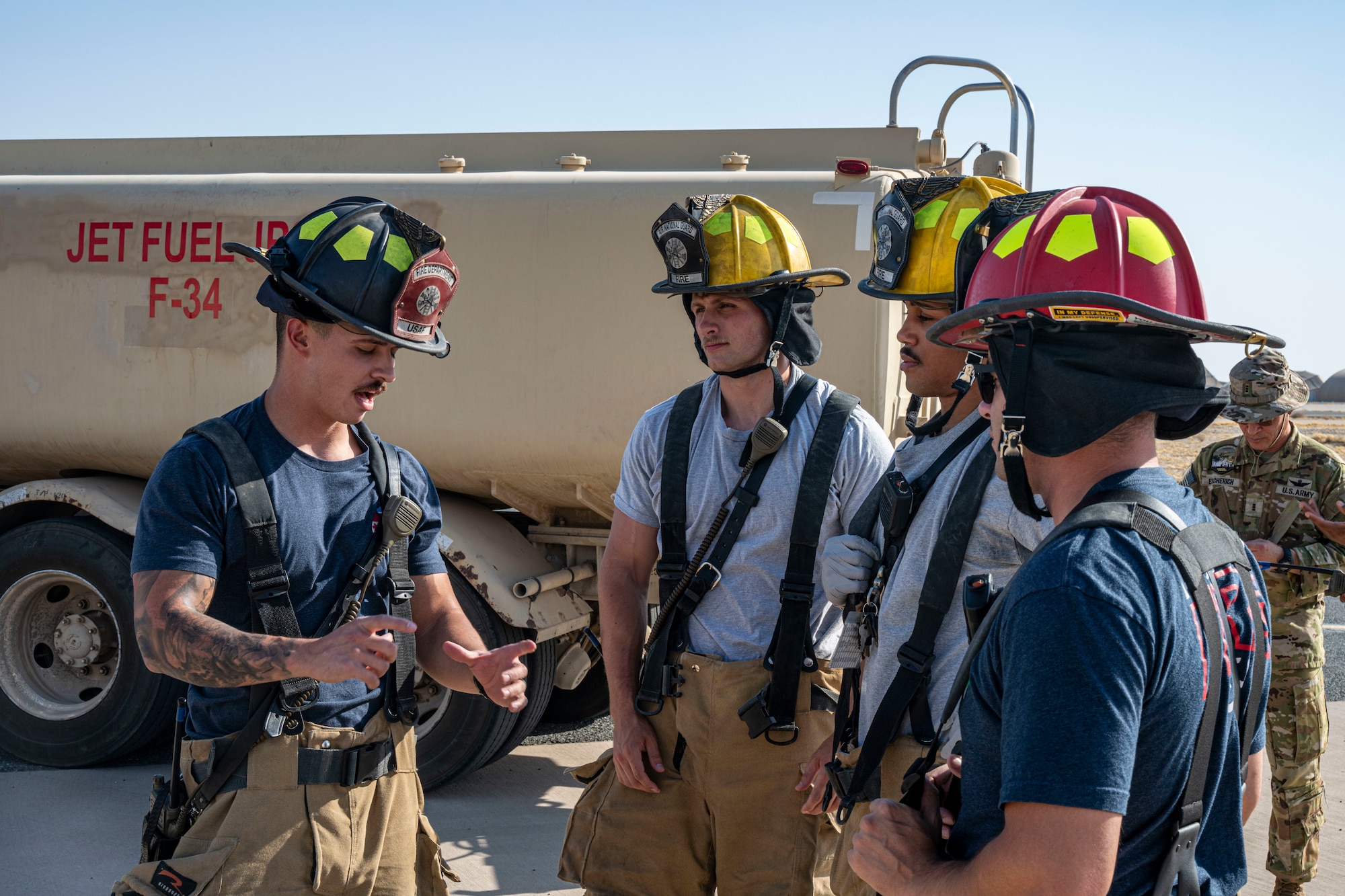 firefighters fill the frame as they discuss procedures in front of a refueler truck