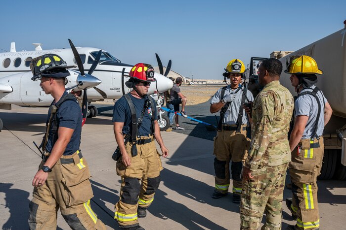 A group of 386th AEW firefighters fill the frame as they discuss procedures in front of a C-12 Huron