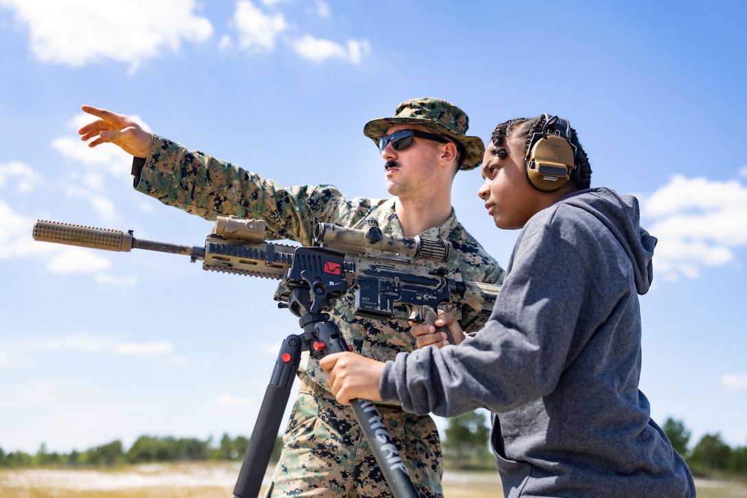 U.S. Marine Corps Cpl. Zachary Matteson, a Florida native, an infantry rifleman with 1st Battalion, 2nd Marine Regiment, 2nd Marine Division, coaches a guest during a family day celebration on Observation Point 2, Marine Corps Base Camp Lejeune, North Carolina, Sept. 12, 2025. V12 hosted a family day celebration to give Marines and Sailors a chance to show their family members a glimpse of their day-to-day duties while also offering hands-on demonstrations of Marine Corps equipment and weapons. (U.S. Marine Corps photo by Lance Cpl. Judith Ann Lazaro)