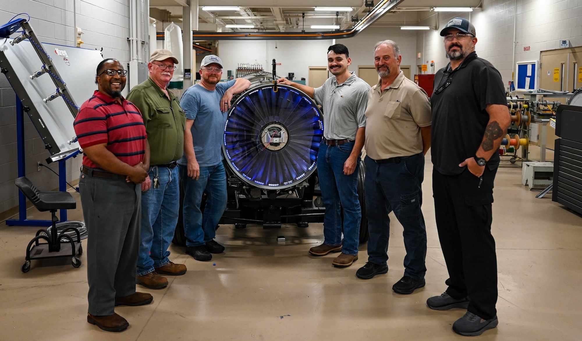 A group of men stand around a plane engine display