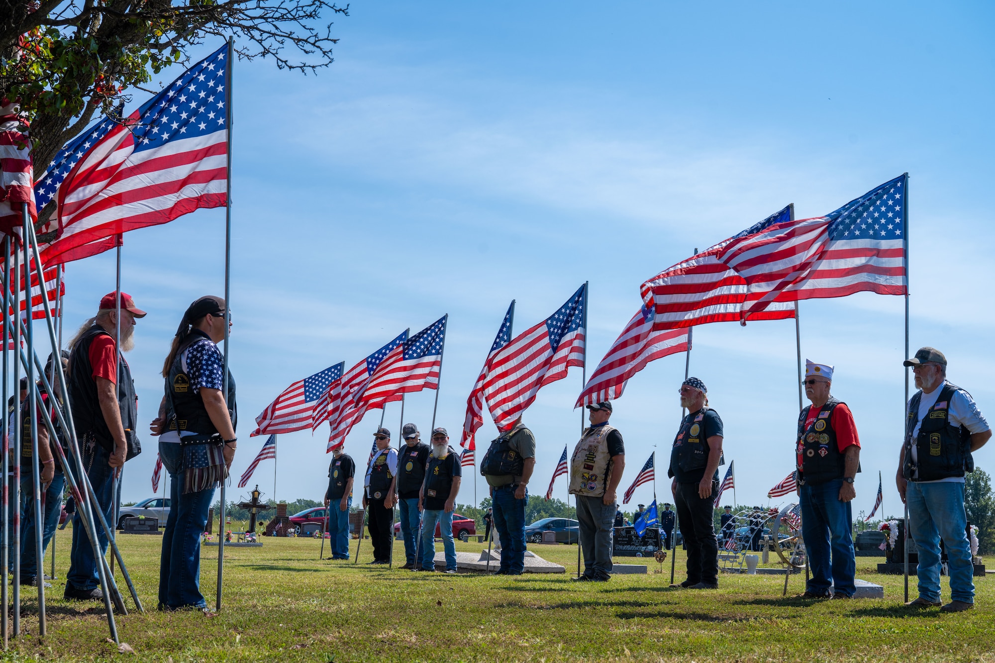 People in leather vests stand in a line holding American flags.