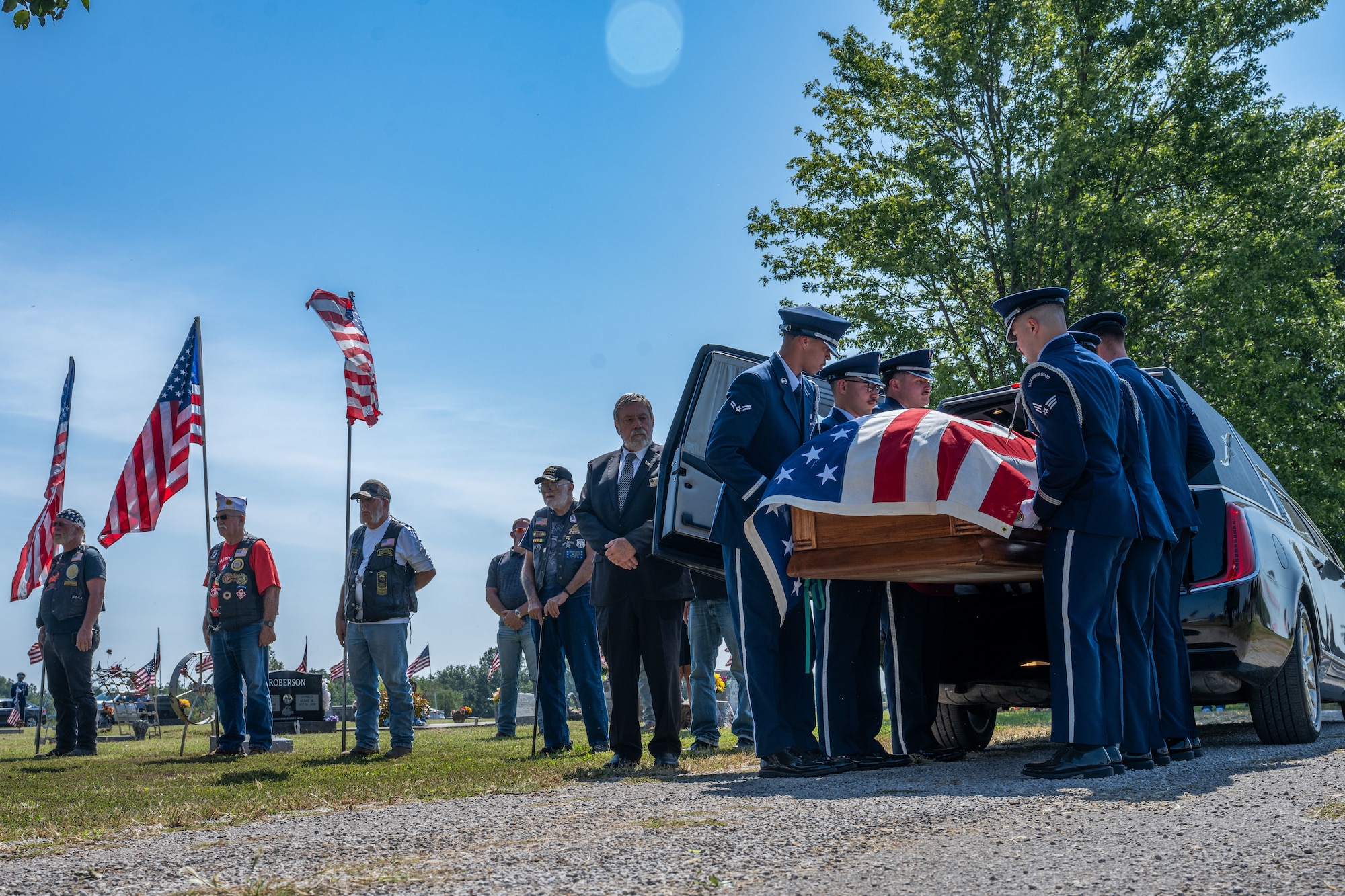 People in military dress uniforms pull a casket draped in an American flag out of a hearse.