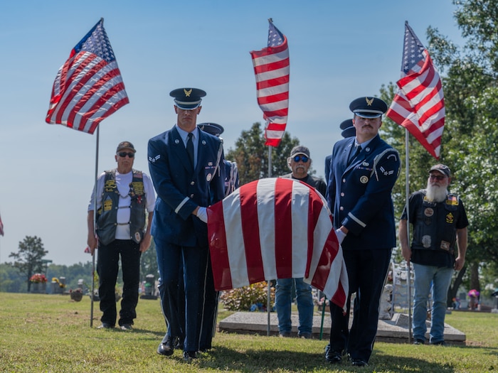 People in military dress carry a casket with an American flag frapped over it.