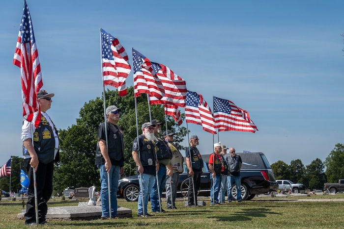 A group of people in leather vests hold American flags.
