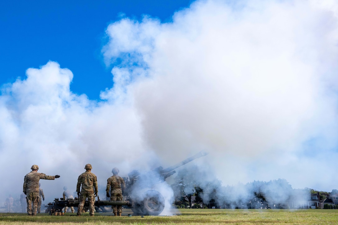 National Guardsmen fire weapons in a field sorrounded by clouds of smoke.