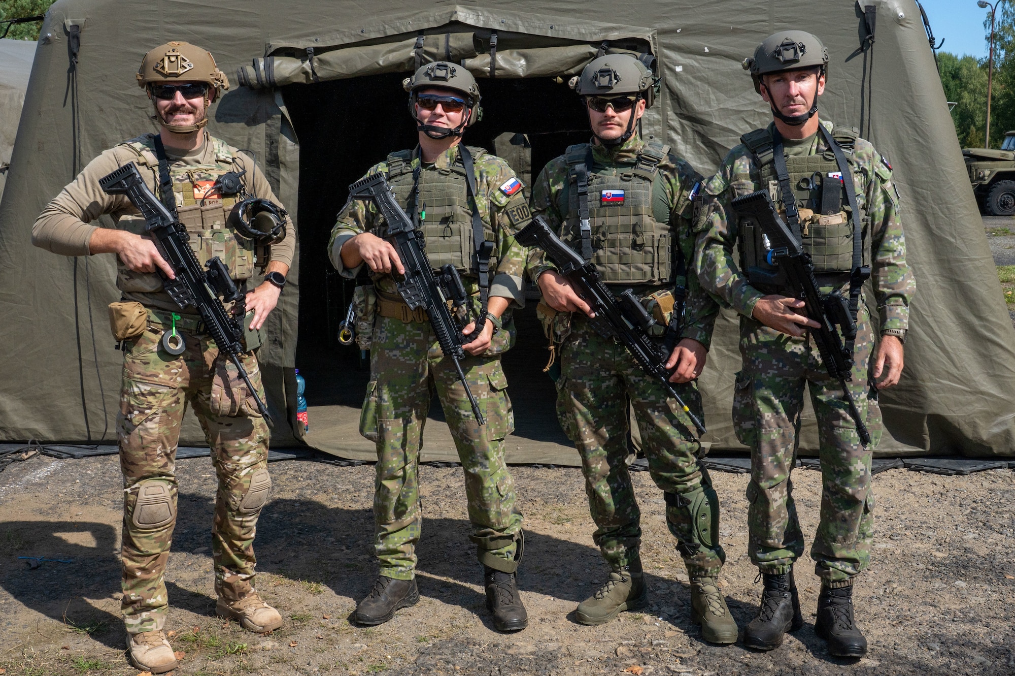 Three members of the Slovak Armed Forces stand in front of a tent with an Airman.