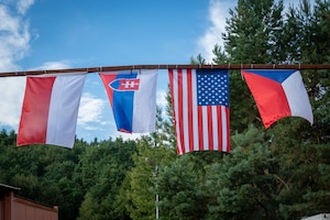 The national flags from Poland, Slovakia, the United States, and the Czech Republic are suspended between two buildings