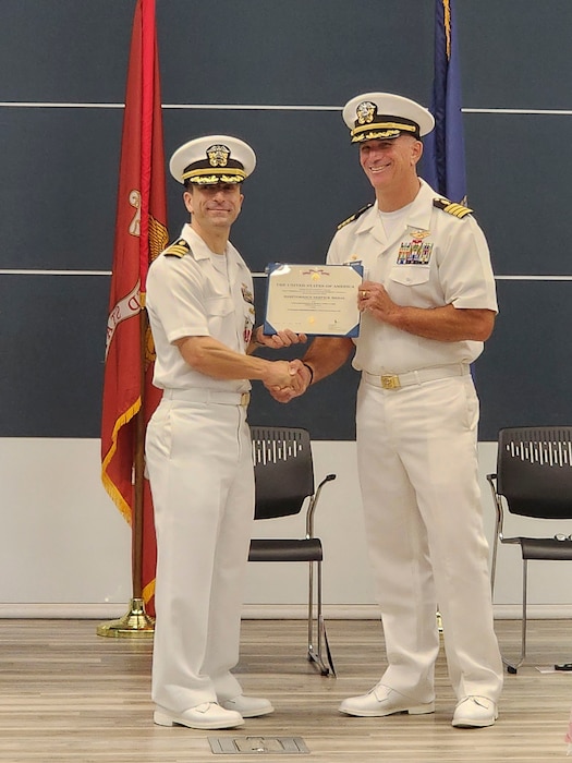 250910-O-NJ594-1179, Bethesda, Maryland, (August 22, 2025) -- Cmdr. Marshall Hoffman, outgoing officer in charge, Navy Bloodborne Infection Management Center, left, is presented with an award by presiding officer Capt. Darryl Arfsten, Commander, Navy and Marine Corps Force Health Protection Command, right, during a change of charge ceremony at United Service Organization (USO) in Bethesda, Maryland, Aug. 22, 2025. The event honored Hoffman’s accomplishments and welcomed Sklar as the new officer in charge, reaffirming the center’s role in medical readiness, force health protection, and compassionate care for service members. (U.S. Navy photo by Ai Marrero)