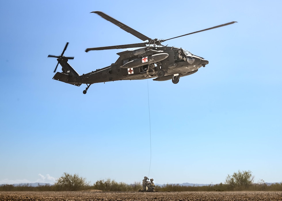 U.S. Army Staff Sgt. Cody Solomon (left), a flight paramedic assigned to Charlie Company, 2nd General Support Aviation Battalion, 1st Aviation Regiment, 1st Combat Aviation Brigade, 1st Infantry Division, secures U.S. Air Force Senior Airman Elias Saavedra (right), 56th Civil Engineer Squadron explosive ordnance disposal technician, into a 420 rescue seat for a hover hoist operation from a moving aircraft